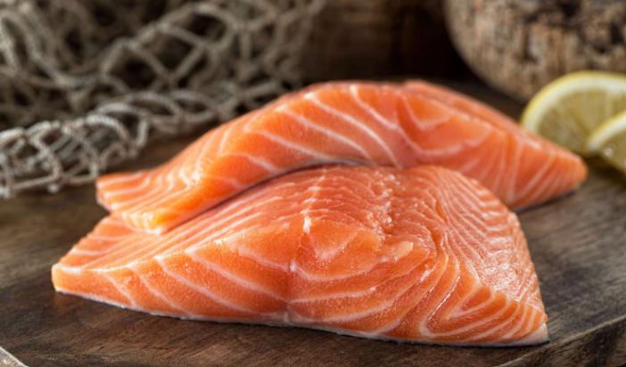 Two raw Atlantic salmon fillets on a wooden board with lemon and fishing net.